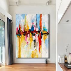 an abstract painting hangs on the wall above a wooden table in a white room with wood flooring