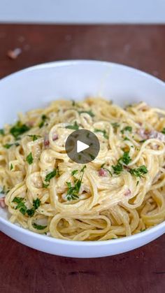 a white bowl filled with pasta on top of a wooden table and topped with parsley