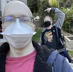 two people wearing face masks in front of a house with one pointing at the camera