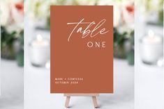 a table sign sitting on top of a wooden easel with candles in the background