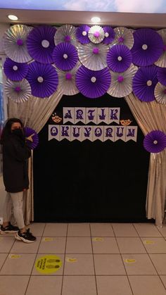 a person standing in front of a purple and white backdrop with paper fans on it