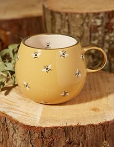 a yellow mug with bees on it sitting on top of a tree stump