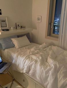 a laptop computer sitting on top of a bed in a room with white sheets and pillows