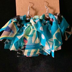 a pair of earrings with blue and green designs on them sitting next to a piece of paper