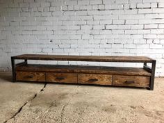 a wooden bench with drawers in front of a white brick wall and concrete flooring