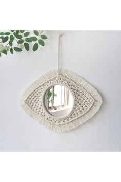 an eye shaped mirror hanging from the side of a white wall next to a potted plant