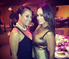 two beautiful women standing next to each other in front of a table with food on it