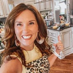 a woman in a leopard print dress is smiling and pointing at the camera while standing in a kitchen