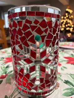 a red mosaic glass vase sitting on top of a table next to a christmas tree