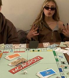 two people sitting at a table with monopoly board game pieces on it and one person holding up the peace sign