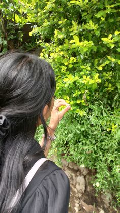 a woman with long black hair looking at bushes