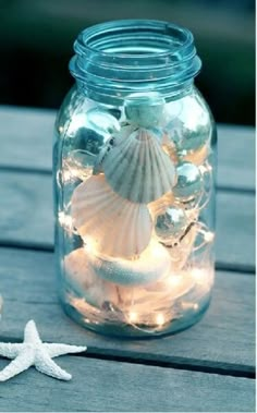 a glass jar filled with sea shells and lights on top of a wooden table next to a starfish