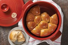 a red pot filled with buns next to a bowl of butter and a spoon