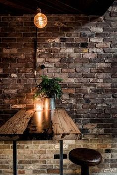 a wooden table topped with a potted plant next to a brick wall and window