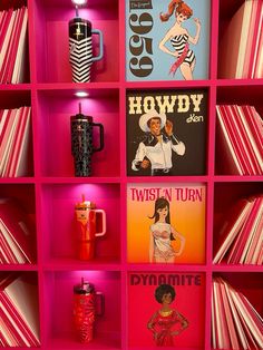 a pink shelf filled with lots of books next to a red cup and drink bottle