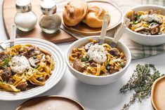 three bowls of pasta with meat, cheese and herbs on the table next to bread rolls