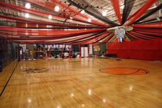 an indoor basketball court with red and white drapes on the ceiling, surrounded by wood flooring