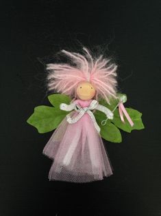 a small doll with pink hair and green leaves on it's back, sitting on a black surface