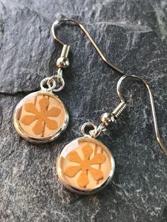 a pair of earrings with an orange flower on them sitting on top of a rock