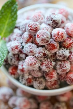 a white bowl filled with powdered sugar covered cranberries next to a green leaf