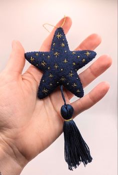 a hand holding a blue and gold star ornament with tassels on it