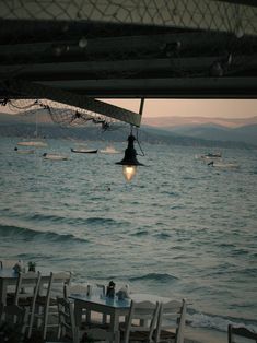 an outdoor dining area overlooking the ocean at dusk with boats in the water and lights hanging from the ceiling