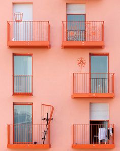 an orange building with balconies and windows on each floor, in front of a pink wall