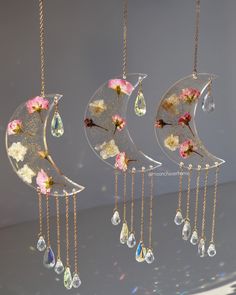 three glass moon wind chimes hanging from chains with flowers and leaves on the side