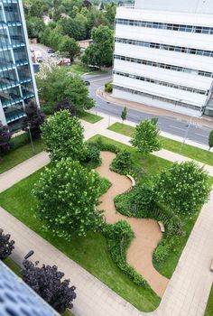 an aerial view of a park with benches and trees in the foreground, surrounded by buildings