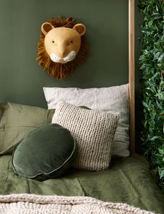 a bed with green sheets, pillows and a lion head on the wall above it