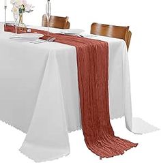 the table is set with two place settings and an orange scarf draped over it's edge