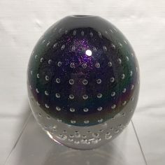 a purple and green glass vase sitting on top of a table next to a white wall