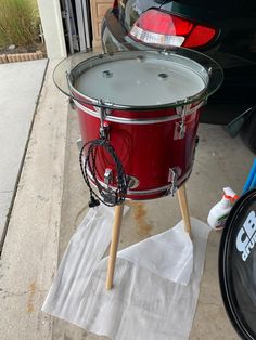 a red drum sitting on top of a piece of paper next to a black car