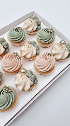 twelve cupcakes with frosting and decorations in a white box on a table