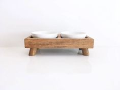 two white bowls in a wooden stand on a white surface with no one around them