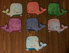 four different colored whale cut outs on a wooden table