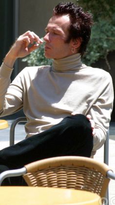 a man sitting at an outdoor table with his hand on his mouth and looking off to the side