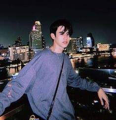 a young man standing on top of a roof next to a cityscape at night