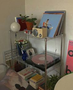 a metal shelf with books, cds and other items on it in a corner next to a chair