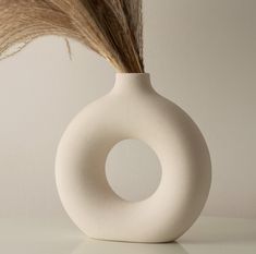 a white vase with some long brown feathers in it's center and the top half of its body