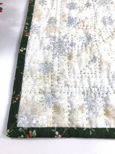 a quilted table runner with snowflakes on it and green trim around the edges