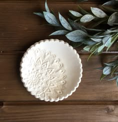 a white plate sitting on top of a wooden table next to green plants and leaves