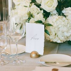 a place setting with white flowers and wine glasses