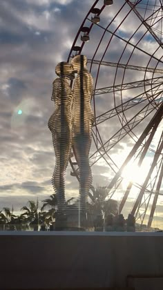 a ferris wheel with two people standing on it's sides and the sun shining behind them