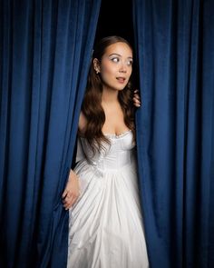 a woman in a white dress peeking out from behind a blue curtain