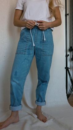 a woman standing in front of a white wall with her hands on her hips and wearing blue jeans