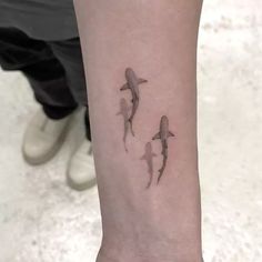 three small sharks on the wrist tattoo by an unknown person's arm, in grey ink