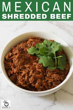 mexican shredded beef in a white bowl with cilantro garnish on top