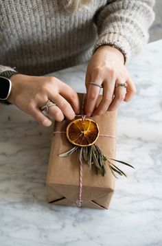 a woman wrapping an orange slice into a brown paper bag with twine on it