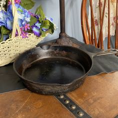 an old frying pan sitting on top of a wooden table next to a basket with flowers